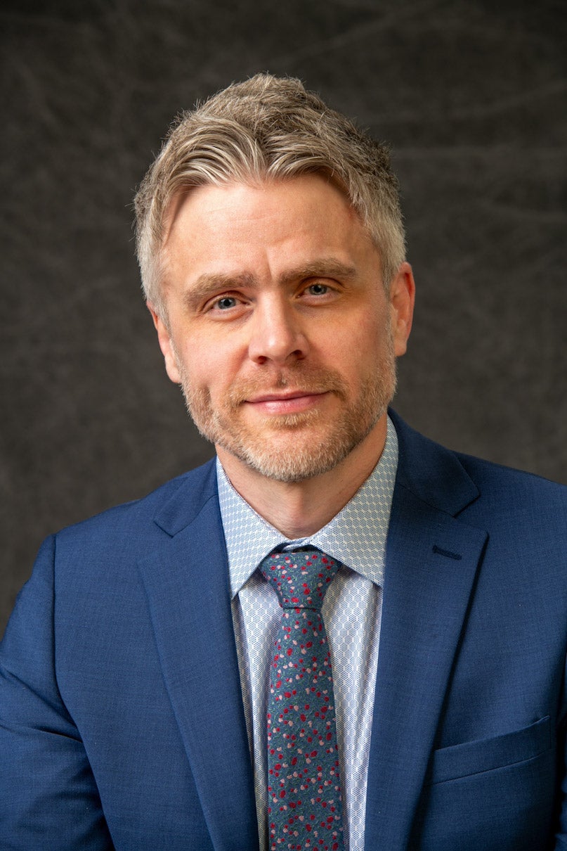 Close up picture of Frank from Chest up wearing a blue suit. Hit tie features red and pink dots
