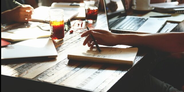 Close up of a scene of people sitting at a table with laptops, notebooks, and drinks