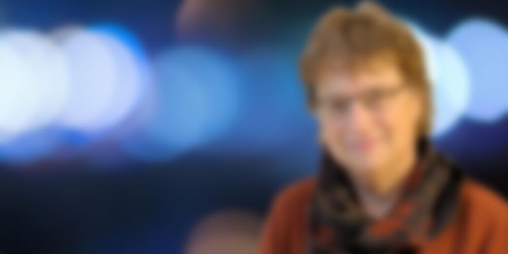 Head shot of Wendy Heller on the right against a background of blurred blue lights