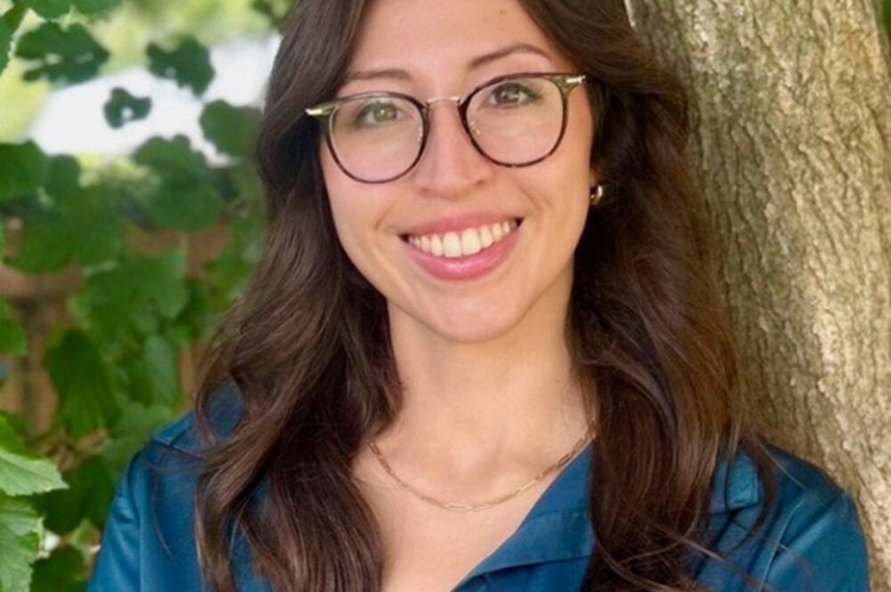 Brenda Straka leaning against a tree in a blue shirt