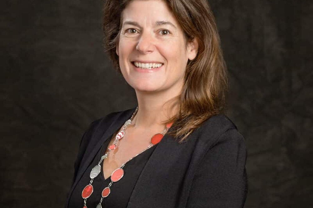 Eva Pomeranz profile picture. Smiling with a dark cardigan sweater in front of a dark background