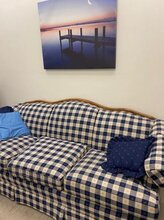 Photograph of a room with a 3-seat couch under a painting of a dock on a lake