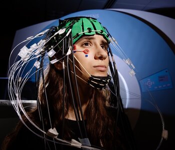 Undergraduate student with an EEG and EROS cap on and sitting in front of an fMRI machine