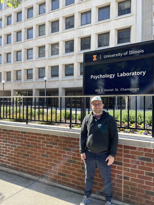 Benedek Kurdi in front of a sign saying “Psychology Laboratory” at the University of Illinois Psychology Department building.