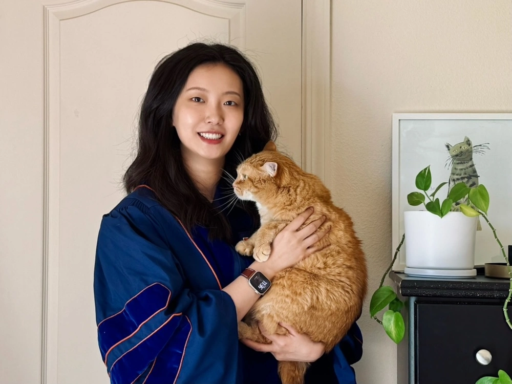 Dr. Yu wearing her doctoral graduation robe and holding an orange cat