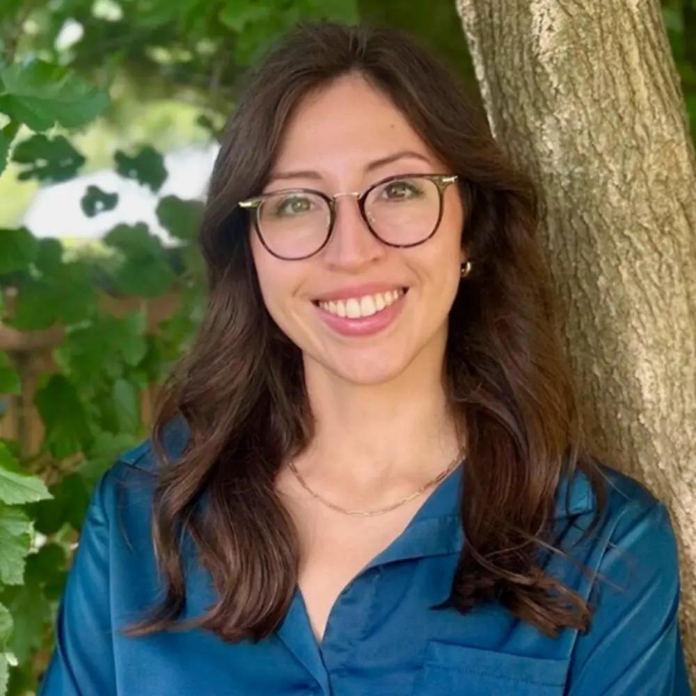 Brenda Straka leaning against a tree in a blue shirt
