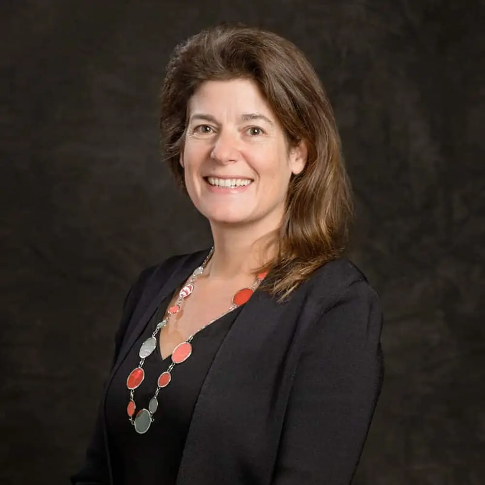 Eva Pomeranz profile picture. Smiling with a dark cardigan sweater in front of a dark background